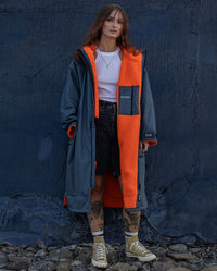 Woman stood in front of dark blue wall, wearing dryrobe Advance Long Sleeve change poncho in Dark Grey Orange