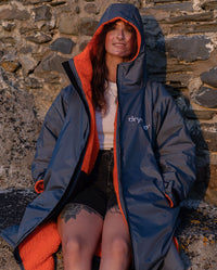 Woman sat on wall in the sun, wearing dryrobe Advance Long Sleeve change poncho in Dark Grey Orange with hood up