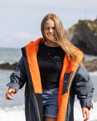 Girl walking on beach towards camera wearing dryrobe Advance Long Sleeve Change poncho in Dark Grey Orange