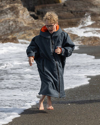 Boy running along shoreline, wearing dryrobe AdvanceLong Sleeve Change robe in Dark Grey Orange