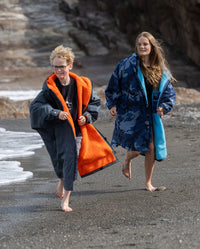 Boy and girl running together on a beach, wearing dryrobe Advance Long Sleeve Change ponchos