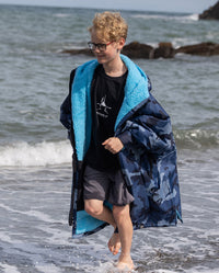 Boy running across shoreline, wearing dryrobe Advance Long Sleeve Changing robe in Blue Camo Blue 