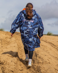 Girl walking up sand dune wearing dryrobe Advance Long Sleeve Changing poncho in Blue Camo Orange