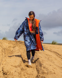 Girl walking down sand dune wearing dryrobe Advance Long Sleeve Changing poncho in Blue Camo Orange