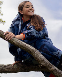 Girl smiling sat in tree, wearing dryrobe Advance Long Sleeve Changing poncho in Blue Camo Orange