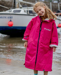 Girl smiling stood in front of boat, wearing dryrobe Advance Long Sleeve Changing poncho in Pink Light Grey 