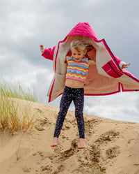 Girl jumping down sand dune, wearing dryrobe Advance Long Sleeve Changing poncho in Pink Light Grey 