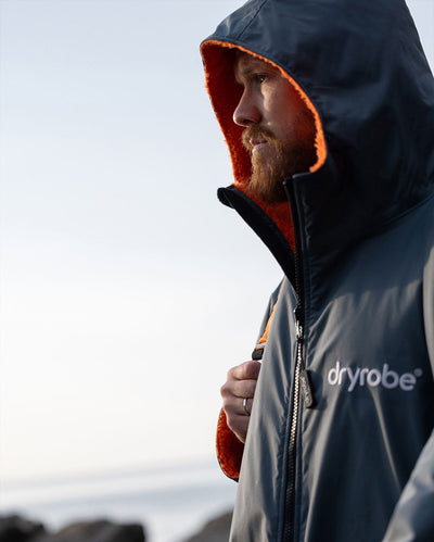 **MALE** Man stood on beach with facing to the side, wearing dryrobe Advance Long Sleeve change robe in Dark Grey Orange