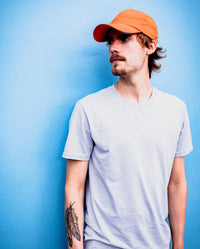 *MALE* Man leaning against a blue wall, wearing Orange dryrobe Quick Dry Cap