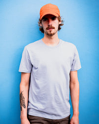 *MALE* Man leaning against a blue wall looking into camera, wearing Orange dryrobe Quick Dry Cap