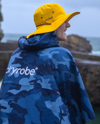 *MALE* Man sat on a beach with back to the camera, wearing dryrobe Quick Dry Brimmed Hat and dryrobe® Waterproof Poncho