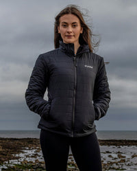 Woman stood on beach on a cloudy day, wearing dryrobe Mid-layer Jacket in Black 