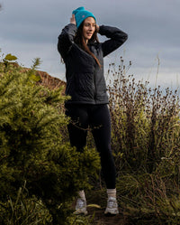 Woman stood in sand dunes, wearing dryrobe Mid-layer Jacket in Black and running gear