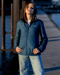 Woman stood in the sun on a pier, wearing dryrobe Mid-layer Jacket in Deep Sea Blue