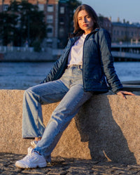 Woman sat in the sun on a wall, wearing dryrobe Mid-layer Jacket in Deep Sea Blue