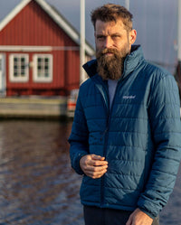 Man stood in front of lake and building, wearing dryrobe Mid-layer Jacket in Deep Sea Blue 