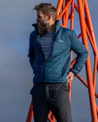 Man wearing dryrobe Mid-layer Jacket in Deep Sea Blue, with blue sky behind him