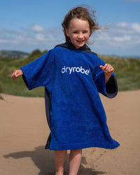 Toddler walking along beach, wearing Kids Organic Towel dryrobe in Blue Grey