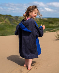 Child walking away from camera on beach, wearing Kids Organic Towel dryrobe in Blue Grey