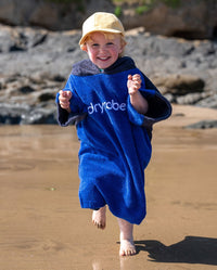 Child running towards camera on beach, wearing Kids Organic Towel dryrobe in Blue Grey