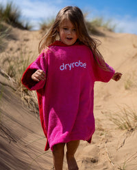 Child running down sand dune, wearing Kids Organic Towel dryrobe in Pink Red