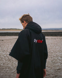 1|Man walking on a beach with back to the camera, wearing Black Grey dryrobe® Advance Short Sleeve