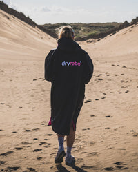 1|Woman walking away from camera through sand dunes, wearing Black Pink dryrobe® Advance Short Sleeve unzipped