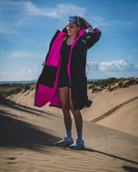 1|Woman stood in running gear in sand dunes, wearing Black Pink dryrobe® Advance Short Sleeve unzipped