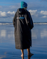 1|Woman walking towards the sea on a beach, wearing Black Blue dryrobe® Advance Long Sleeve