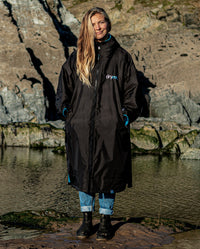 1|Woman stood on beach in front of rocks, wearing Black Blue dryrobe® Advance Long Sleeve