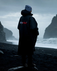Person stood on stormy coastline facing the sea, wearing Black Grey dryrobe® Advance Long Sleeve