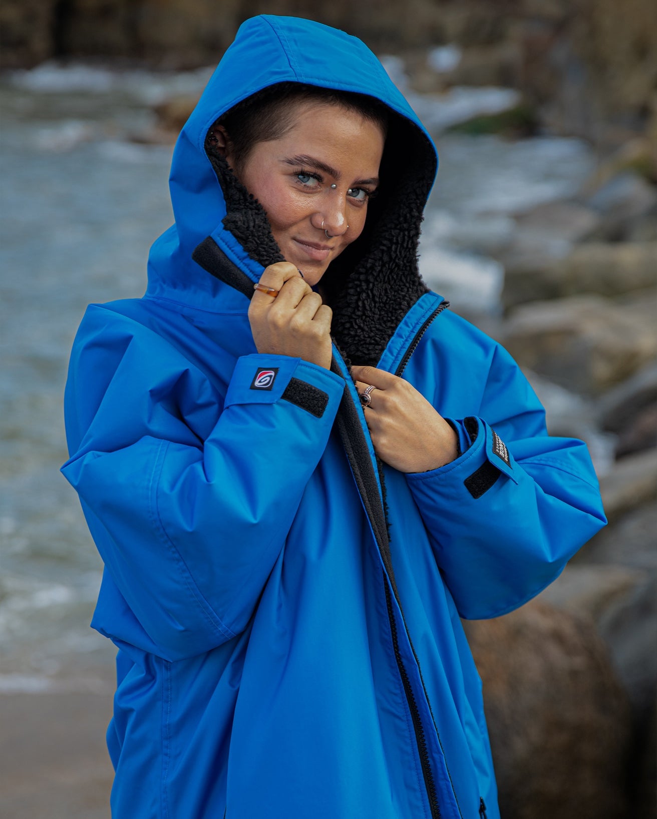 Close up of woman stood on a beach, wearing Cobalt Blue Black dryrobe® Advance Long Sleeve with hood up