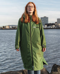 Woman with glasses stood in front of sea, wearing Forest Green dryrobe® Advance Long Sleeve