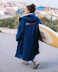 1|Woman walking along road carrying a yellow surfboard, wearing  Navy Grey dryrobe® Advance Long Sleeve