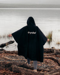 Woman walking towards lake with back to the camera, wearing Black dryrobe® Waterproof Poncho