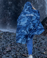 Woman with back to camera walking towards a waterfall, wearing  Blue Camo dryrobe® Waterproof Poncho 