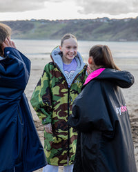 1|Three girls stood on beach talking, wearing dryrobe® Advance Kids Long Sleeve