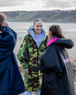Three girls stood on beach talking, wearing Kids dryrobe® Advance Long Sleeve changing poncho