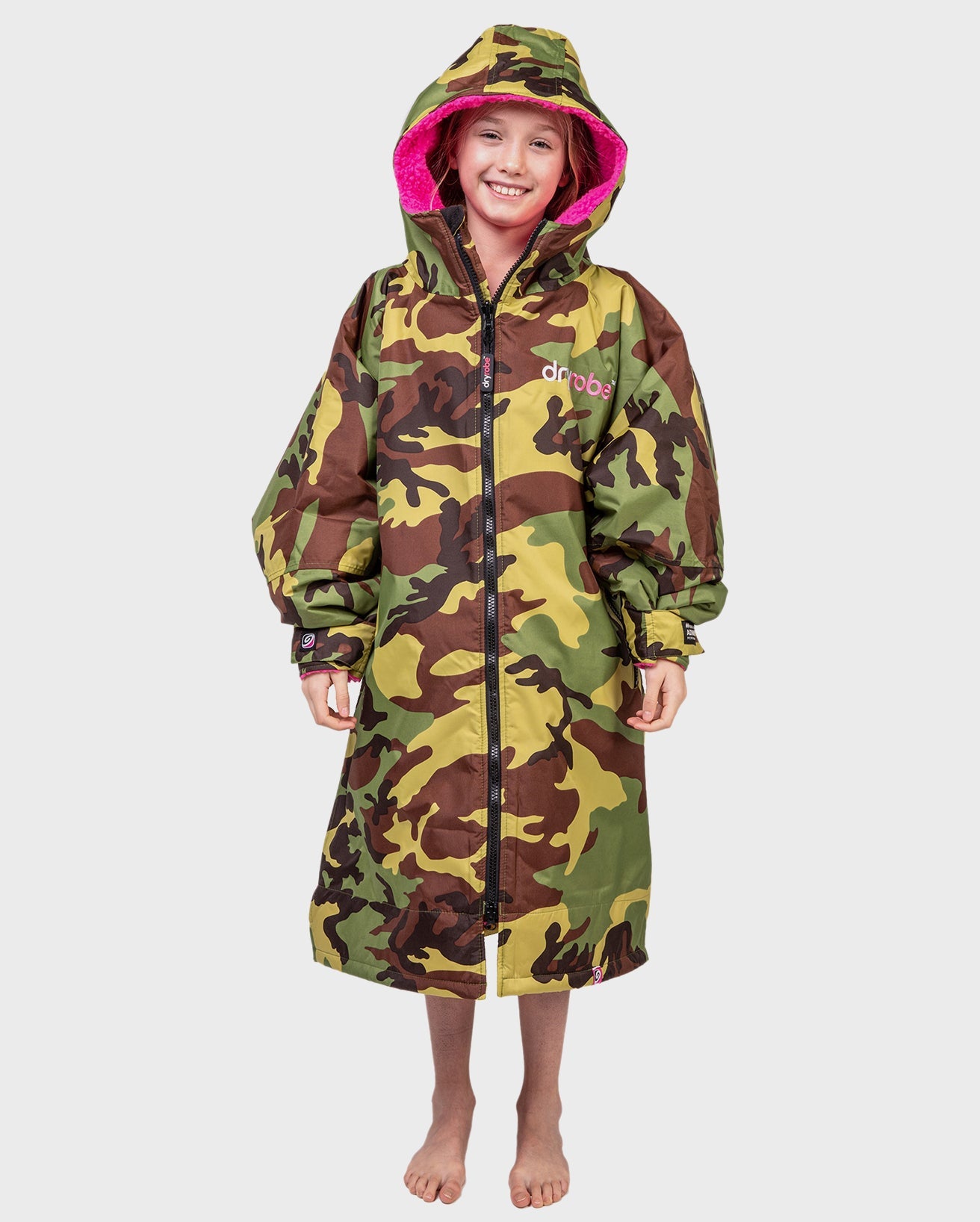 1|Girl smilng wearing Camo Pink dryrobe® Advance Kids Long Sleeve with hood up