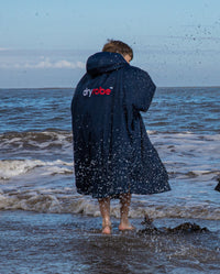 1|Boy stood in sea facing away from camera wearing Navy Grey dryrobe® Advance Kids Long Sleeve