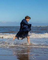 1|Boy running through shoreline wearing Navy Grey dryrobe® Advance Kids Long Sleeve