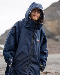 1|Boy stood in the rain on a beach wearing Navy Grey dryrobe® Advance Kids Long Sleeve with hood up 