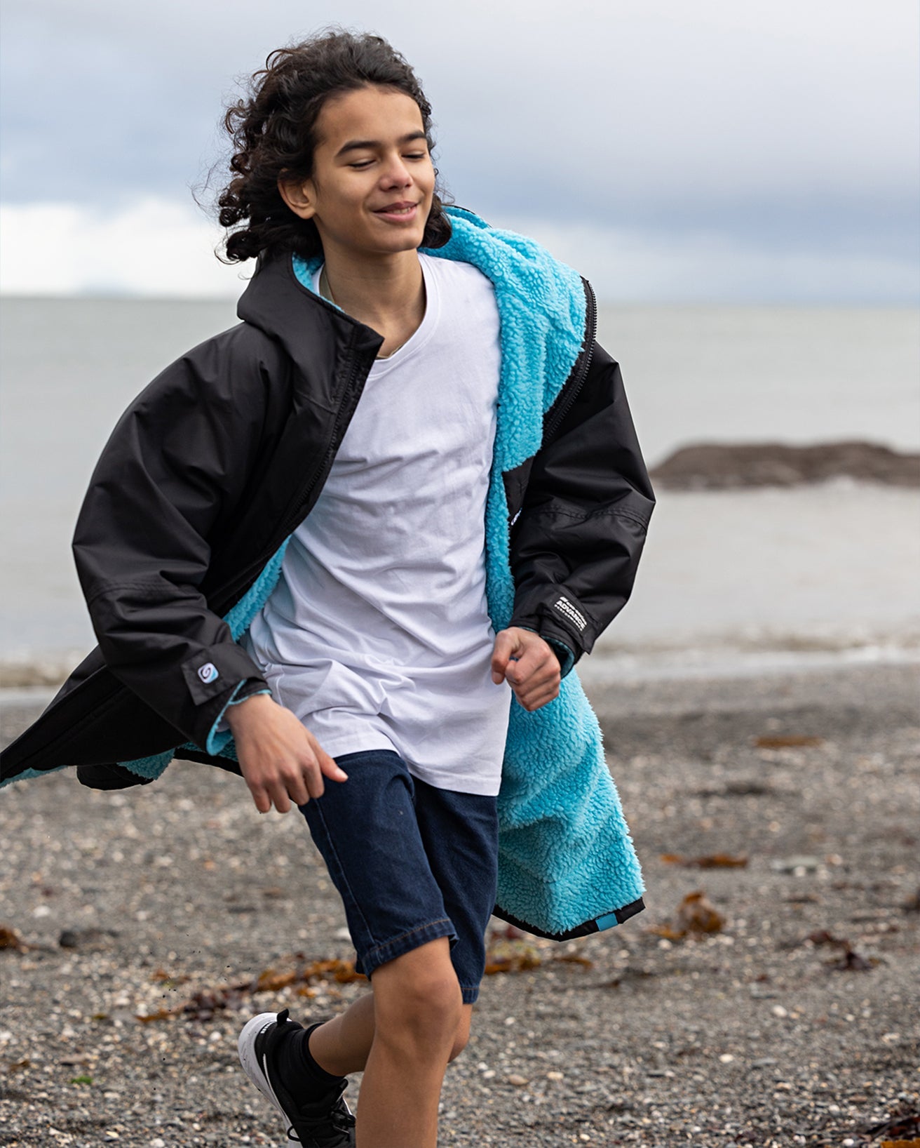 1|Boy running on a beach, wearing Black Blue dryrobe® Advance Kids Long Sleeve