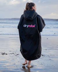 1|Girl walking towards the sea wearing Black Pink dryrobe® Advance Kids Long Sleeve