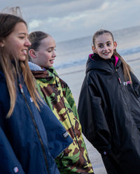 1|Three girls walking along a beach, wearing dryrobe® Advance Kids Long Sleeve