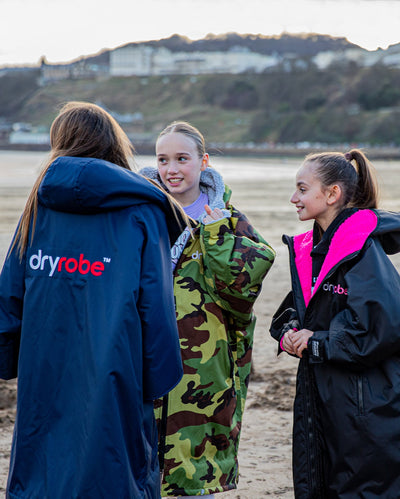 Three girls chatting on the beach, wearing Kids dryrobe Advance change ponchos