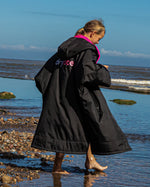 Girl stood by the sea wearing Black Pink dryrobe® Advance Kids Short Sleeve change poncho