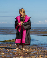 Girl stood in front of the sea looking to the left, wearing Black Pink dryrobe® Advance Kids Short Sleeve change poncho