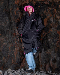 *MALE* leaning against rocks, wearing Black Pink dryrobe® Advance Long Sleeve with hood up