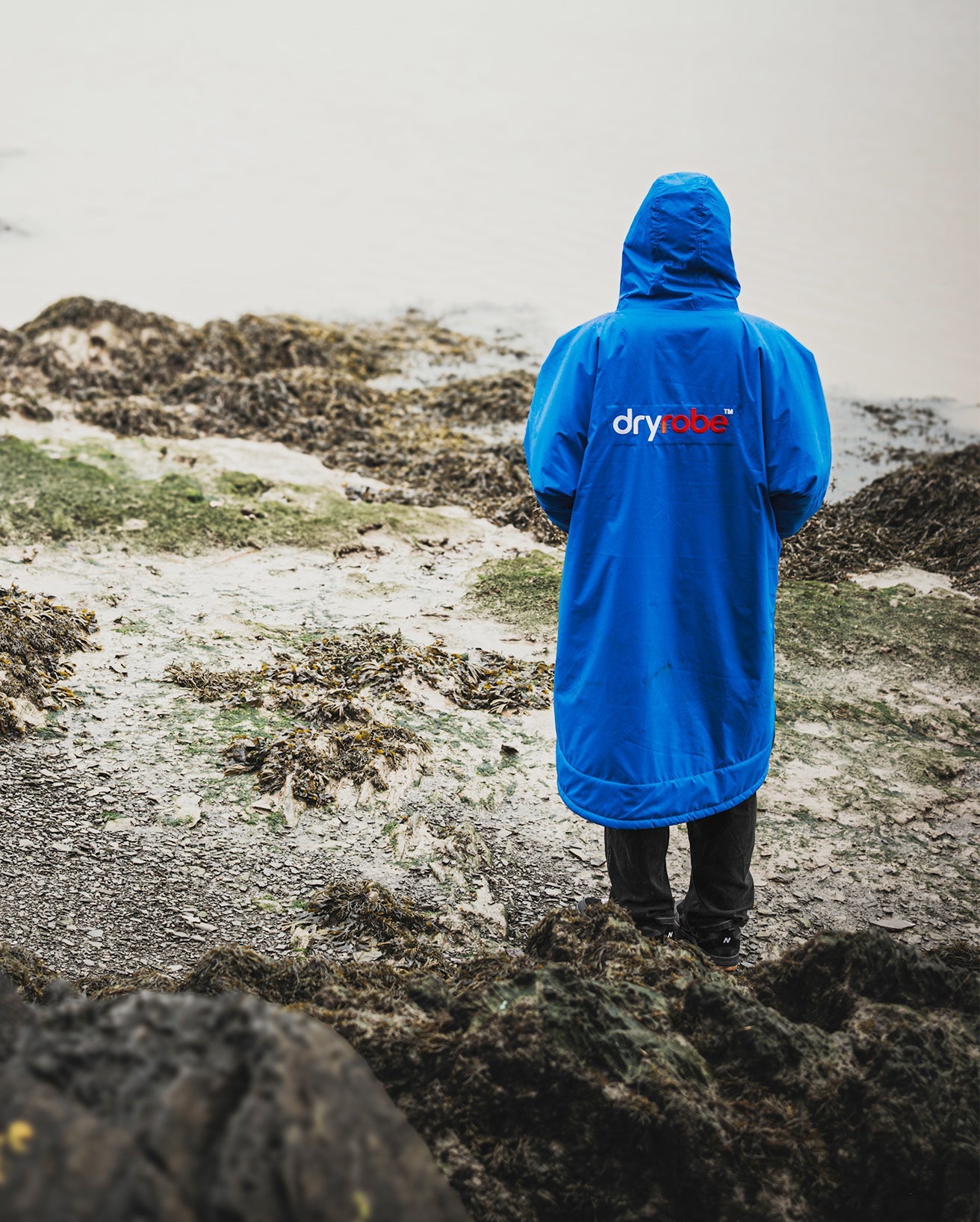 *MALE* standing on a beach with back to the camera, wearing Cobalt Blue Black dryrobe® Advance Long Sleeve